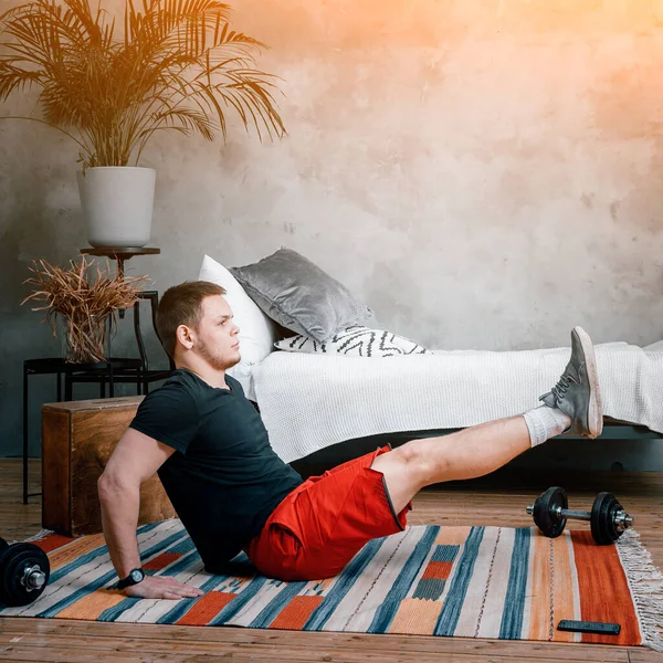 若い男は家でスポーツに行き オンラインで訓練する 選手はプレスを作ってベッドルームに足を持ち上げ — ストック写真