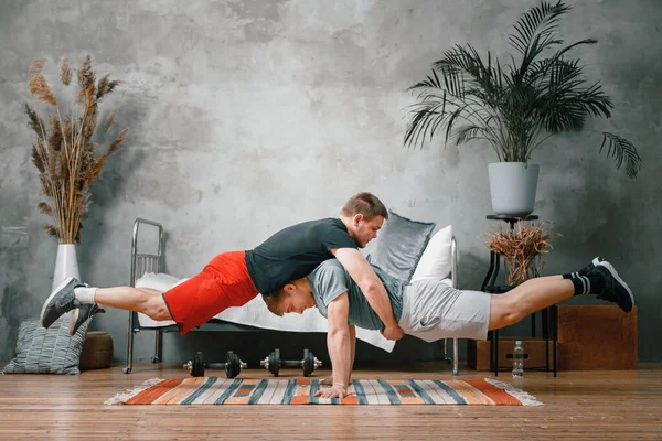 選手の男性は ベッド カーペットを背景に ベッドルームでお互いに板を作ります 体操選手の訓練アクロバットのホームトリック — ストック写真