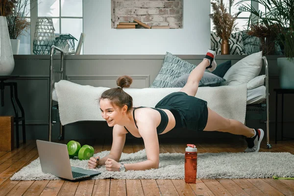 若い女性は自宅でスポーツのために行きます オンライントレーニング 選手は脚を振り ベッドルームのラップトップから映画や研究を見ます — ストック写真