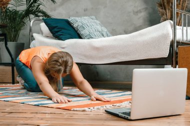 Genç bir kadın spor için eve gidiyor, online antrenman. Sporcu esniyor, meditasyon yapıyor, yatak odasında yerde oturuyor.