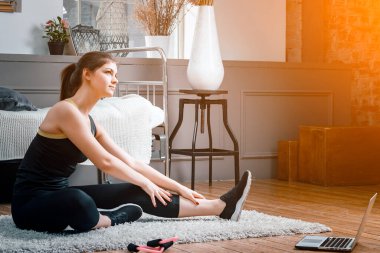 Güzellik kraliçesi spor için eve gider. Kızıl saçlı neşeli, sportif kadın yatak odasında bacağına kadar uzanıyor.