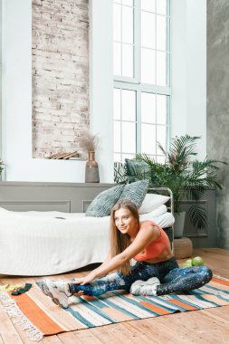 Genç bir kadın spor için eve gidiyor, online antrenman. Sporcu esniyor, meditasyon yapıyor, yatak odasında yerde oturuyor.