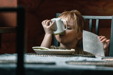 Mutfakta iki yaşında küçük bir çocuk mutfaktaki yemek masasındaki bebek içicisinden su içiyor.