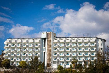 Kırık camlı eski bir otel binası, sokakta bir asansör, tropikal bir ülkede, parlak gökyüzüne karşı palmiye ağaçları olan klimalar ve tabelalar.