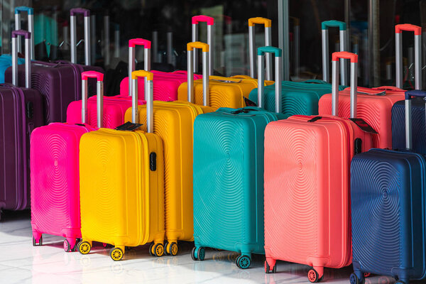 Ярко-синий, розовый, желтые ряды чемоданов с расширенными ручками и различных размеров в продаже перед магазином