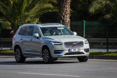 Antalya, Türkiye 12 Nisan 2021: Beyaz Volvo XC90 sıcak bir yaz gününde bir palmiye ağacının zeminine doğru hızla sürüyor 