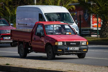 Antalya, Türkiye 12 Nisan 2021: Kırmızı pikap Isuzu Campo sıcak bir yaz gününde palmiyelerin arkasına doğru hızla sürüyor  