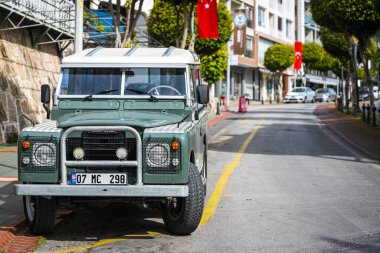 Antalya, Türkiye 12 Nisan 2021: Yeşil Land Rover Defender sıcak bir yaz gününde ağaçların, palmiyelerin önüne park etti 