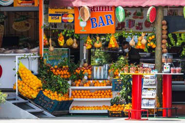 Alanya, Türkiye 12 Nisan 2021: Turuncu, çilek, muz, mandalina, ananas, hindistan cevizi, nar gibi taze yerel meyvelerle dolu bir sokak marketi. Satıcı meyveden taze meyve suyu yapar. 