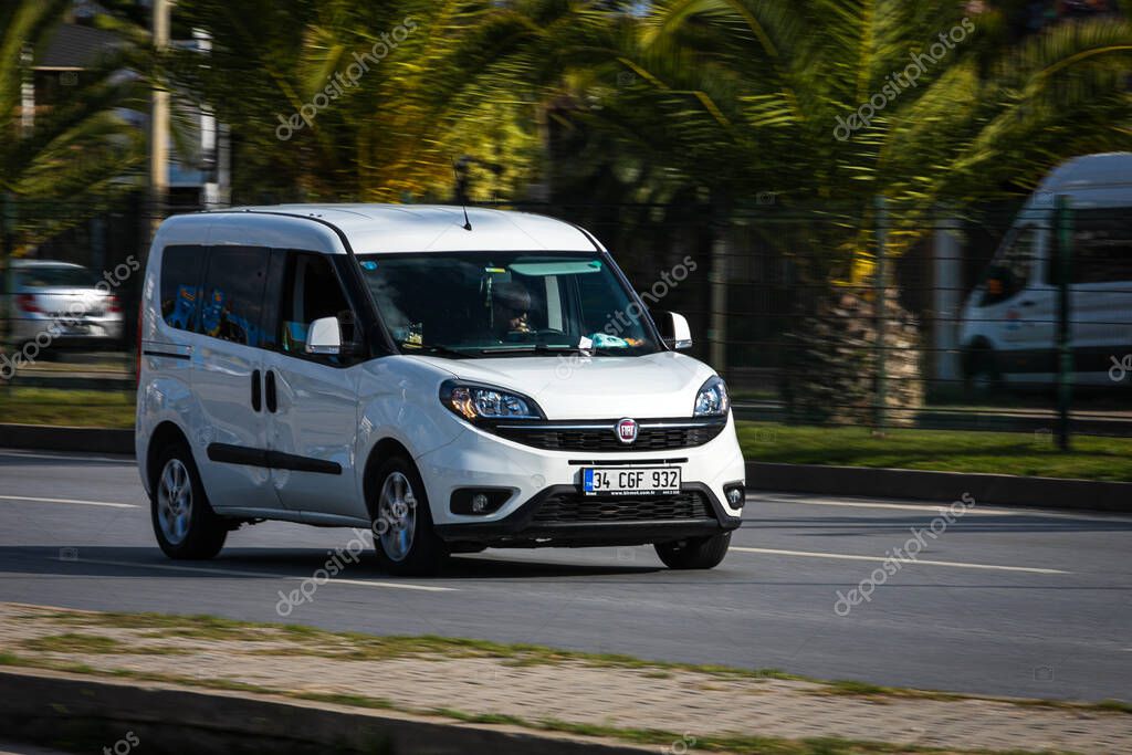 Alanya, Turkey  April 12 2021:   white Fiat Doblo  is driving fast on the street on a warm summer day against the backdrop of a  palms