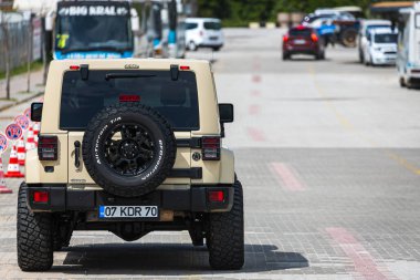 Alanya, Türkiye 12 Nisan 2021: Bej rengi Jeep Wrangler sıcak bir yaz gününde park alanının arka planına park etti.  