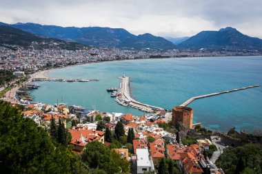 Kırmızı tuğladan kale kulesi olan bir rıhtımın üst görüntüsü güzel beyaz bir deniz feneri ve mavi denizin arka planında bir sürü tekne ve yat olan bir rıhtım.