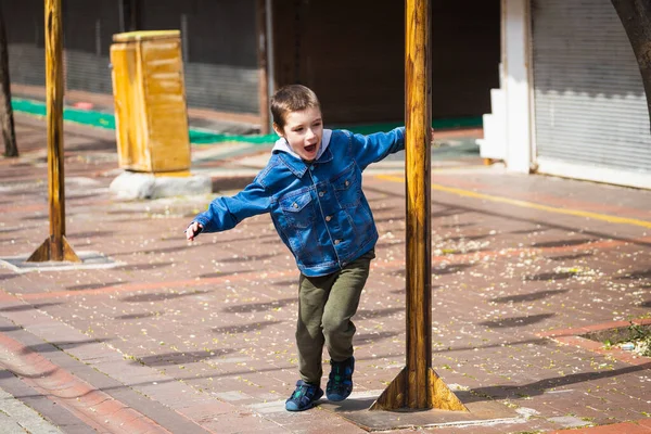 デニムジャケットの男の子が陽気に叫び 暖かい日に街の通りのポールの周りを旋回します — ストック写真