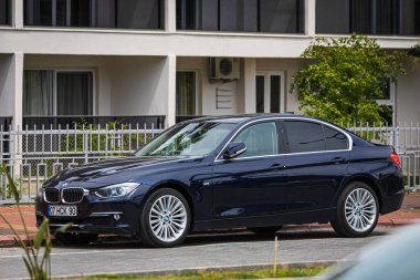 Alanya, Türkiye 12 Nisan 2021: Siyah BMW 5 serisi sıcak bir yaz gününde bir binanın arka planına, avuç içlerine park edildi 