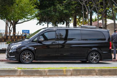 Alanya, Türkiye 12 Nisan 2021: Siyah Mercedes-Benz Vito sıcak bir yaz gününde bir binanın arka planına, avuç içlerine park etti 