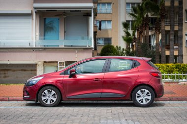 Alanya, Türkiye 12 Nisan 2021: Kırmızı Renault Clio sıcak bir yaz gününde bir binanın arka planına, palmiyelere karşı sokağa park edildi 