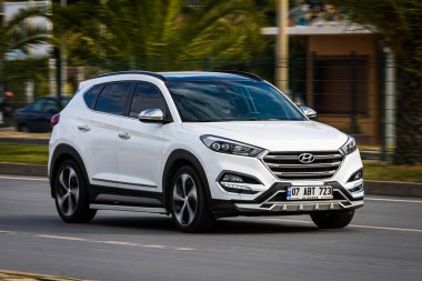 Alanya, Türkiye 13 Nisan 2021: Beyaz Hyundai Tucson sıcak bir yaz gününde palmiyelerin arkasına doğru hızla sürüyor  