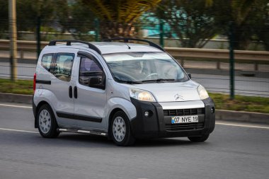Alanya, Türkiye 13 Nisan 2021: Gümüş CITROEN BERLINGO sıcak bir yaz gününde palmiyelerin arka planına doğru hızla sürüyor  