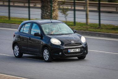 Alanya, Türkiye 13 Nisan 2021: Siyah Nissan Micro sıcak bir yaz gününde palmiyelerin arkasına doğru hızla sürüyor  