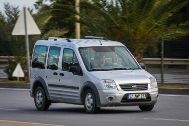 Alanya, Türkiye 13 Nisan 2021: Gümüş Ford Transit Connect sıcak bir yaz gününde bir palmiye ağacının zeminine doğru hızla sürüyor  