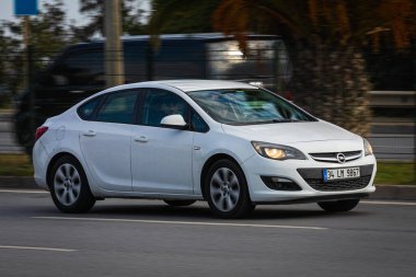 Alanya, Türkiye 13 Nisan 2021: Beyaz Opel Astra sıcak bir yaz gününde palmiyelerin arkasına doğru hızla sürüyor  