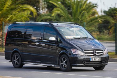 Alanya, Türkiye 13 Nisan 2021: Siyah Mercedes-Benz Vito sıcak bir yaz gününde bir palmiye ağacının arka planına doğru hızla sürüyor  