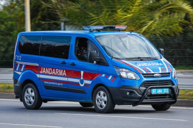 Alanya, Türkiye 13 Nisan 2021: Mavi Ford Transit Jandarma sıcak bir yaz gününde bir palmiye ağacının arka planına doğru hızla sürüyor   