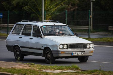 Alanya, Türkiye 13 Nisan 2021: Beyaz Renault 12, sıcak bir yaz gününde palmiyelerin arkasına doğru hızla sürüyor  