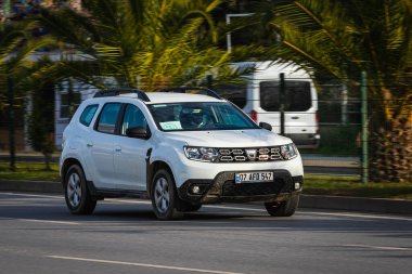 Alanya, Türkiye 13 Nisan 2021: Beyaz Renault DUSTER sıcak bir yaz gününde palmiyelerin arkasına doğru hızla sürüyor  