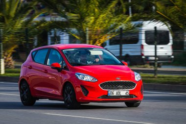 Alanya, Türkiye 13 Nisan 2021: Kırmızı Ford Fiesta sıcak bir yaz gününde palmiyelerin arkasına doğru hızla sürüyor  