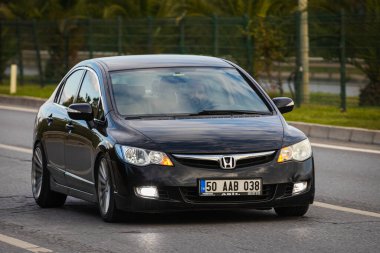 Alanya, Türkiye 13 Nisan 2021: Siyah Honda Civiç sıcak bir yaz gününde palmiyelerin arkasına doğru hızla sürüyor  