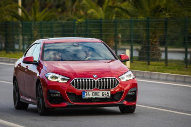 Alanya, Türkiye 13 Nisan 2021: Kırmızı BMW 2 serisi sıcak bir yaz gününde palmiyelerin arkasına doğru hızla ilerliyor  