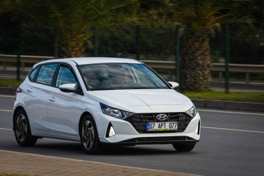 Alanya, Türkiye 13 Nisan 2021: Beyaz Hyundai i20 sıcak bir yaz gününde palmiyelerin arkasına doğru hızla sürüyor  