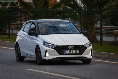Alanya, Türkiye 13 Nisan 2021: Beyaz Hyundai i20 sıcak bir yaz gününde palmiyelerin arkasına doğru hızla sürüyor  