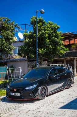 Alanya, Türkiye 15 Nisan 2021: Siyah Honda Civiç sıcak bir yaz gününde ağaçların, palmiyelerin önüne park etti 