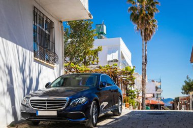 15 Nisan 2021: Siyah Mercedes-Benz E-sınıfı sıcak bir yaz gününde bir binanın arka planına, avuç içlerine park edilmiştir. 