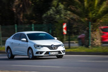 Alanya, Türkiye 16 Nisan 2021: Beyaz Renault Megane sıcak bir yaz gününde bir palmiye ağacının arka planında hızlı sürüyor 