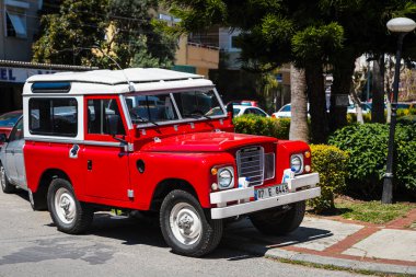 Alanya, Türkiye 17 Nisan 2021: Kırmızı Land Rover Defender sıcak bir yaz gününde ağaçların, palmiyelerin önüne park etti 
