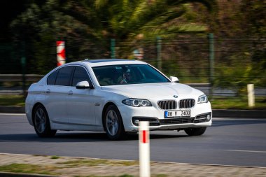 Alanya, Türkiye 13 Nisan 2021: Beyaz BMW 5 serisi sıcak bir yaz gününde bir palmiye ağacının zeminine doğru hızla ilerliyor 