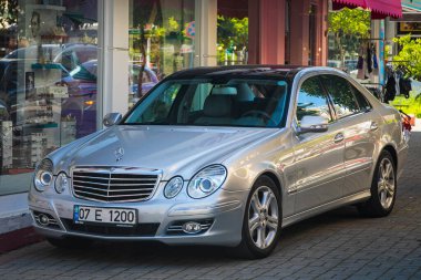 Alanya, Türkiye 17 Nisan 2021: Gümüş Mercedes-Benz E-sınıfı sıcak bir yaz gününde bir binanın, ağaçların, dükkanların zeminine karşı sokağa park edildi 