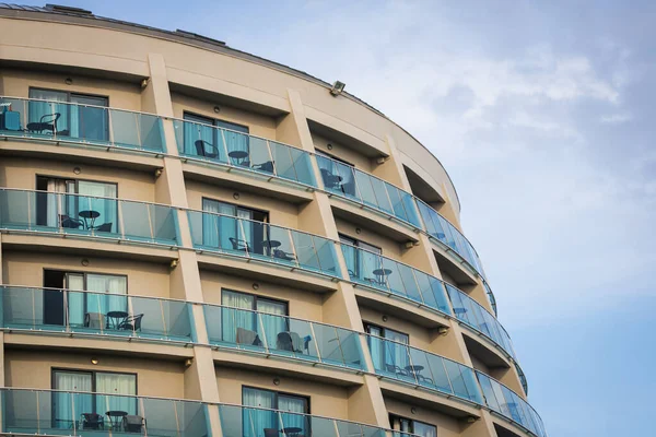 A residential building with flat, identical balconies with ripped air conditioners and  glass. Balcony pattern