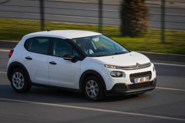 Alanya, Türkiye 17 Nisan 2021: Beyaz Citroen C3 sıcak bir yaz gününde bir palmiye ağacının arka planına doğru hızla sürüyor  