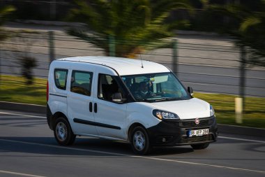 Alanya, Türkiye 17 Nisan 2021: Beyaz Fiat Duplo sıcak bir yaz gününde palmiyelerin arkasına doğru hızla sürüyor  