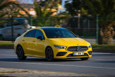 Alanya, Türkiye 17 Nisan 2021: Sarı Mercedes-Benz CLA sınıfı sıcak bir yaz gününde palmiyelerin arka planına doğru hızla sürüyor  