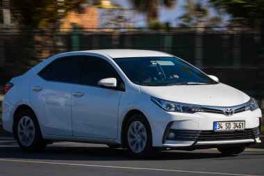 Alanya, Türkiye 17 Nisan 2021: Beyaz Toyota Corolla sıcak bir yaz gününde bir palmiye ağacının arka planında hızlı sürüyor  