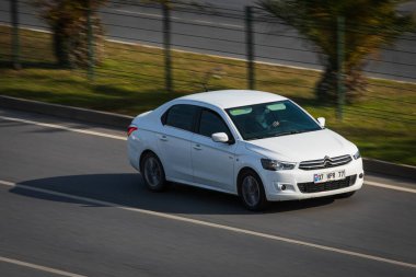 Alanya, Türkiye 17 Nisan 2021: Beyaz Citroen C-Elysee sıcak bir yaz gününde palmiyelerin arka planına doğru hızla sürüyor  