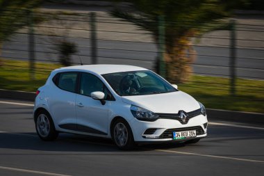 Alanya, Türkiye 17 Nisan 2021: Beyaz Renault Clio sıcak bir yaz gününde palmiyelerin arkasına doğru hızla sürüyor  