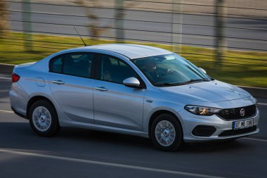 Alanya, Türkiye 17 Nisan 2021: Beyaz Fiat Albea sıcak bir yaz gününde palmiyelerin arkasına doğru hızla sürüyor  