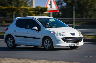 Alanya, Türkiye 18 Nisan 2021: Beyaz Peugeot 308 sıcak bir yaz gününde bir palmiye ağacının arka planında hızlı sürüyor  