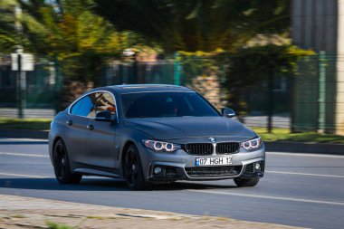 Alanya, Türkiye 17 Nisan 2021: Gümüş renkli BMW 4 serisi sıcak bir yaz gününde palmiyelerin arka planına doğru hızla ilerliyor  